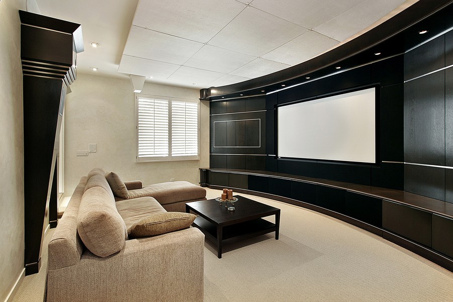  A media room with a large projector screen on a black wall. There is a sectional and a black table.
